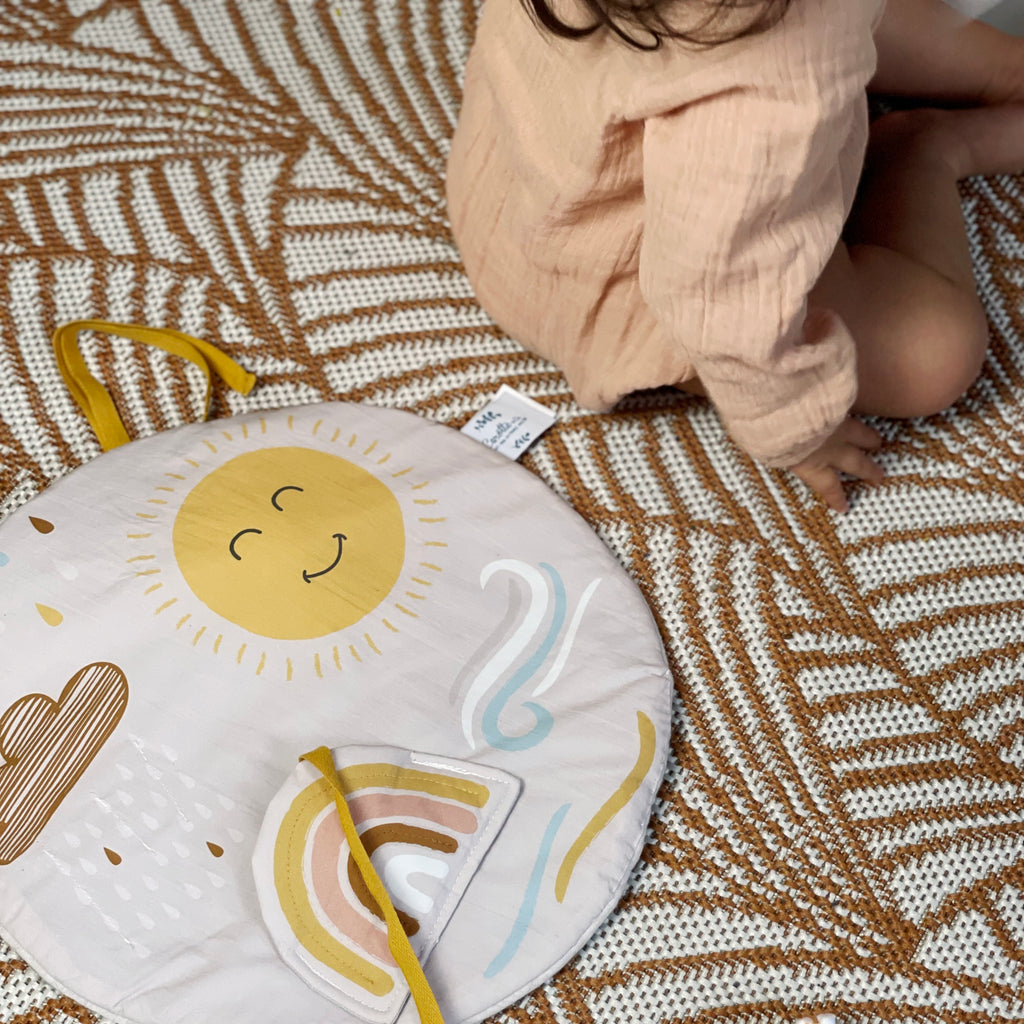 bébé joue avec son tableau d'éveil en tissu aux motifs inspirés de la météo dessiné et fabriqué en France par Carotte & Cie