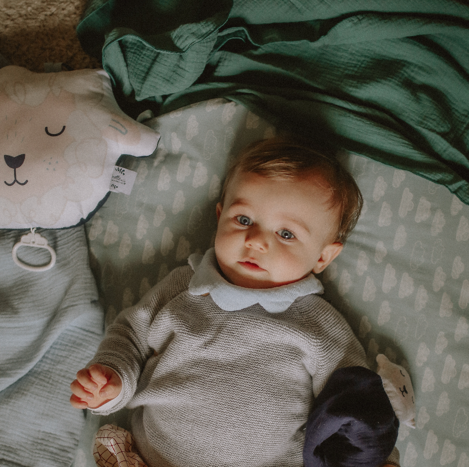 bébé jouant avec un coussin illustré au motif mouton blanc, beige et bleu dessiné et fabriqué par Carotte & Cie