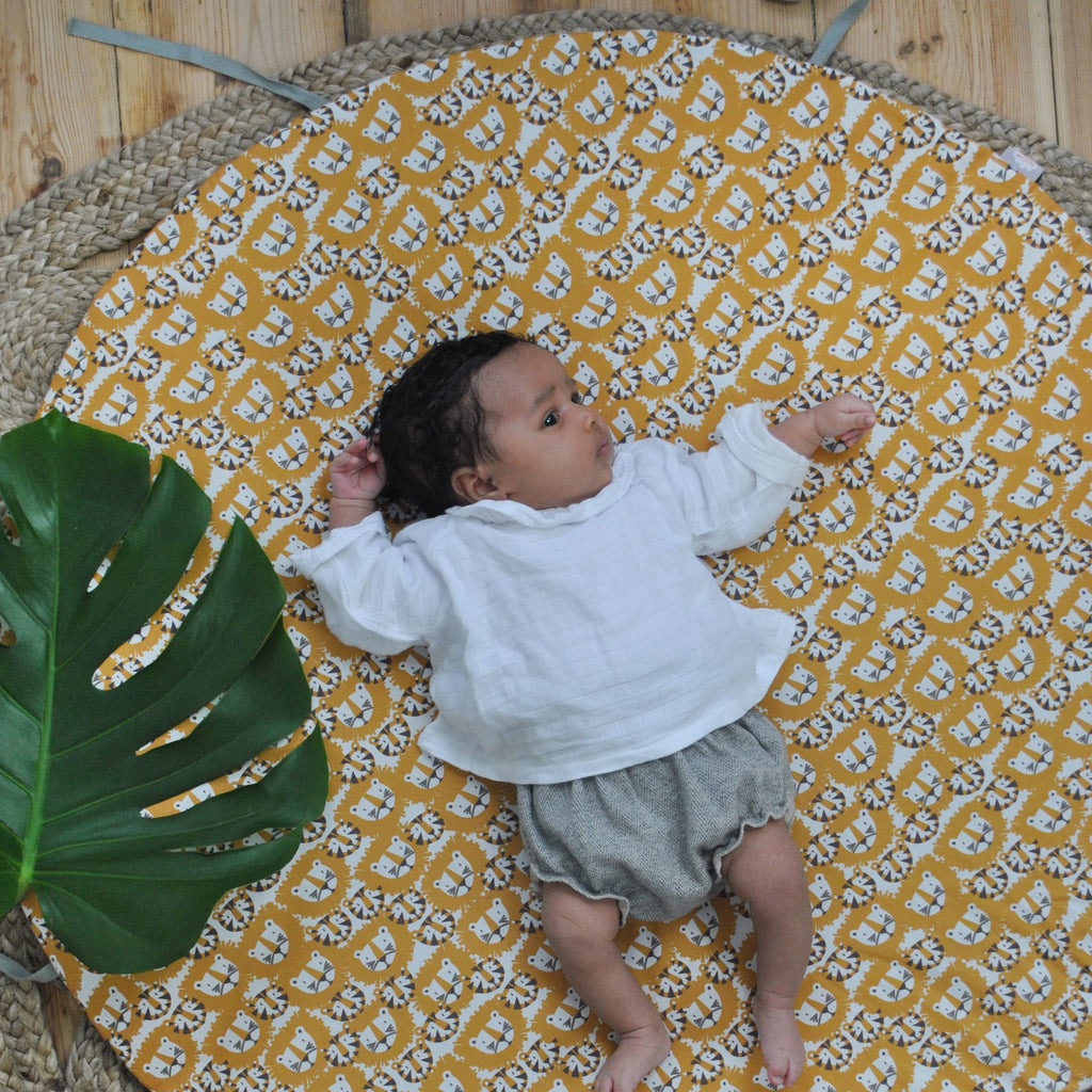 bébé est confortablement installé sur son tapis de jeu rond moelleux avec liens pour le transformer en panier de rangement pour jouets motif tigres et lions orange et marron Carotte & Cie