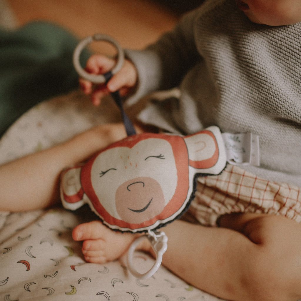 Bébé joue avec son petit coussin musical singe rouge dessiné et fabriqué en France par Carotte & Cie