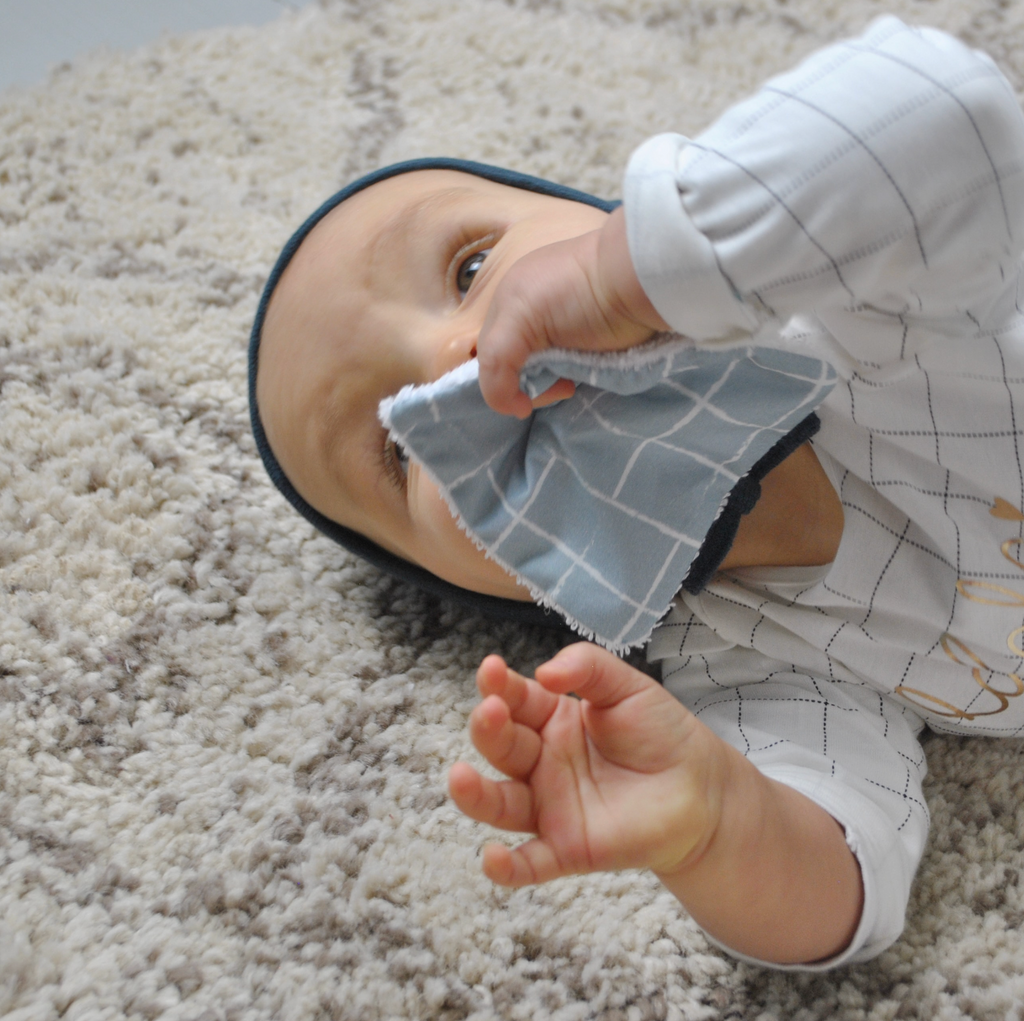 Bébé joue avec une lingette lavable en coton bio motif carreaux bleu céladon dessiné et fabriqué par Carotte & Cie