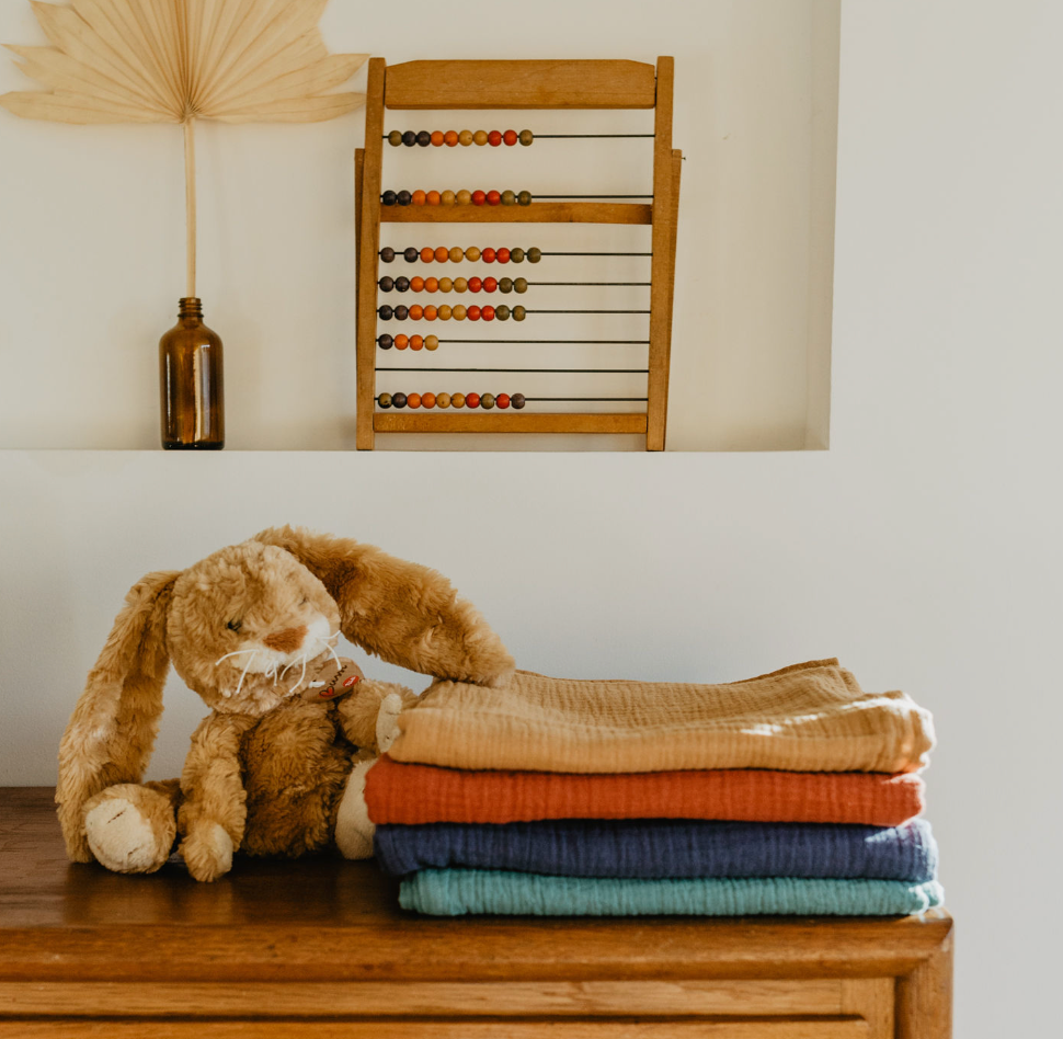 ambiance d'une chambre d'enfant avec une pile de maxi langes uni en gaze de coton camel, rouge terracotta, bleu marine et vert eucalyptus dimensions 100 X 100 cm réalisé par Carotte & Cie