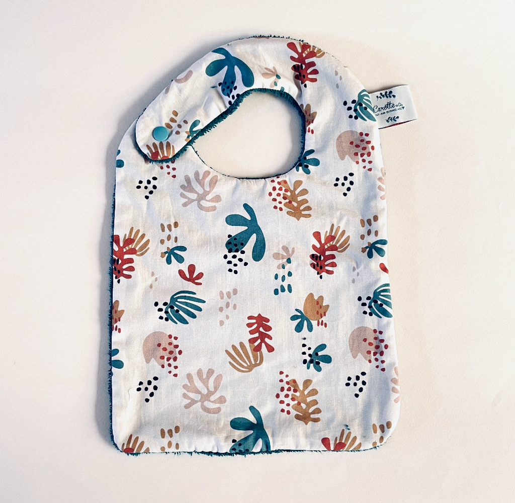 Grand bavoir motif corail multicolore sur fond beige rosé et dos éponge bleu canard Carotte & Cie