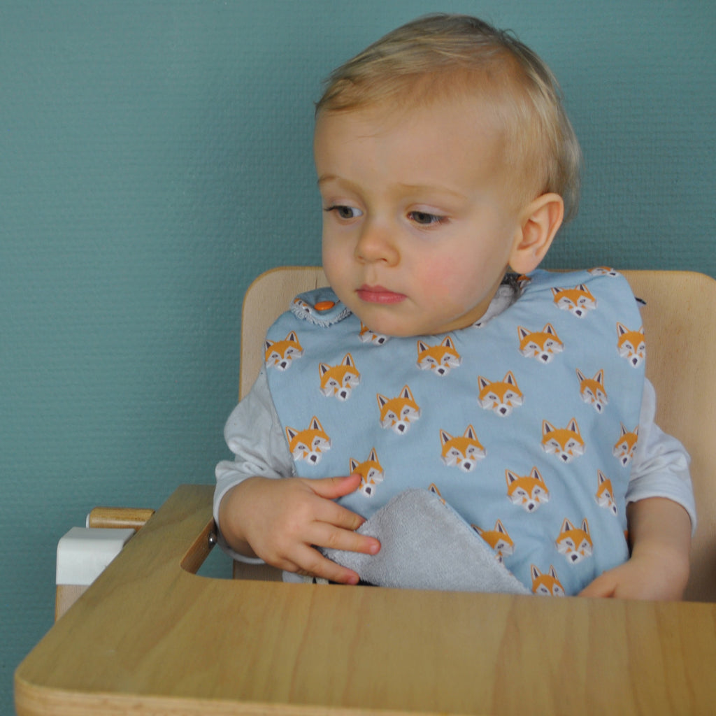 Bébé porte son bavoir en coton biologique motif exclusif renards bleu et éponge grise
 Carotte & Cie