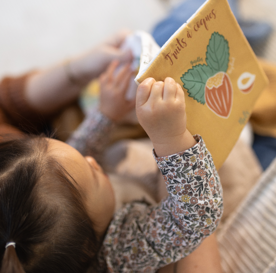 bébé lit son livre d'éveil les familles de fruits une face coloriée et une autre noir et blanc pour l'éveil de bébé dessiné avec amour par Carotte & Cie