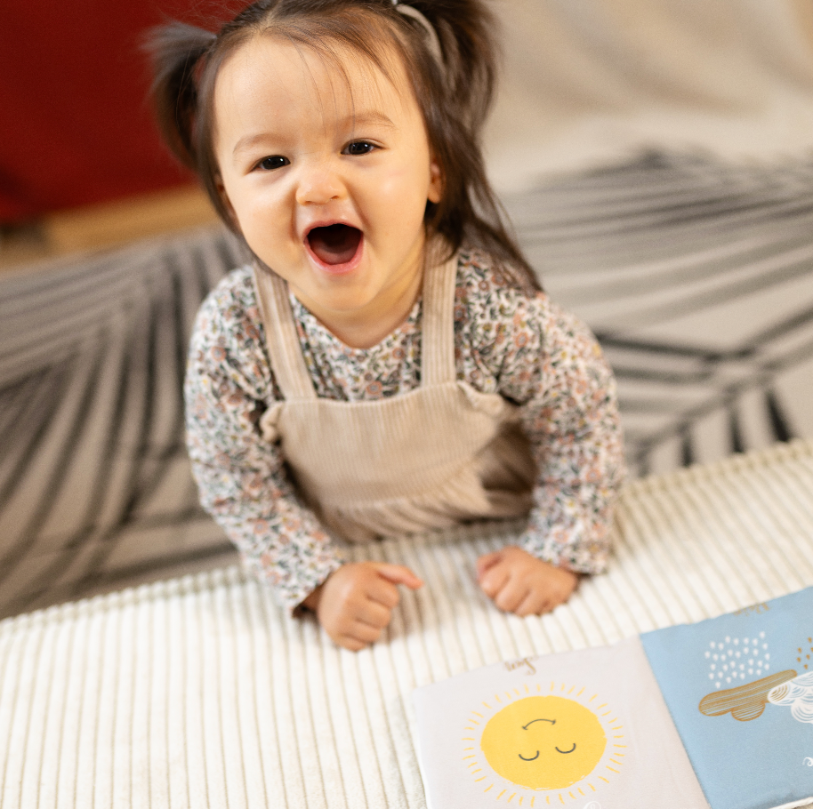 bébé joue avec son livre d'éveil la météo une face coloriée et une autre noir et blanc pour l'éveil de bébé dessiné avec amour par Carotte & Cie