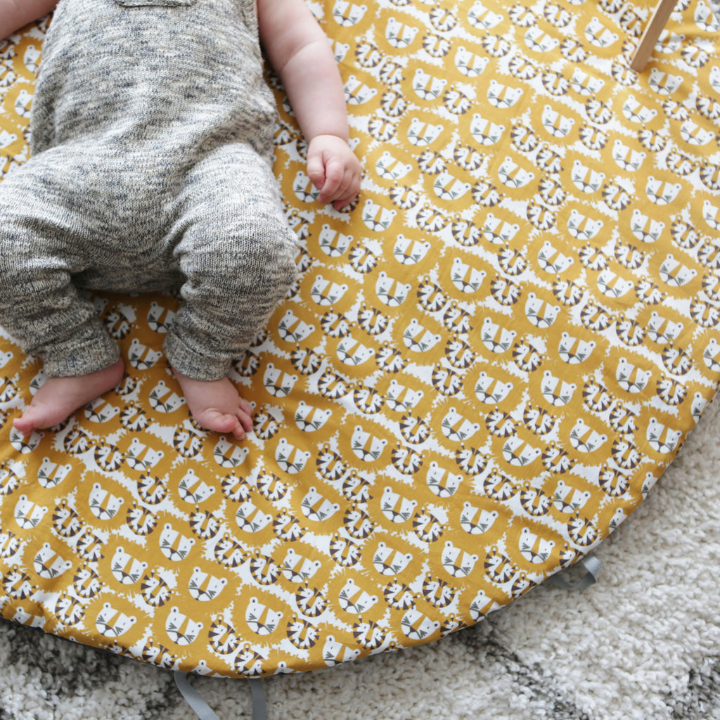bébé est confortablement installé sur son tapis de jeu rond moelleux avec liens pour le transformer en panier de rangement pour jouets motif tigres et lions orange et marron Carotte & Cie