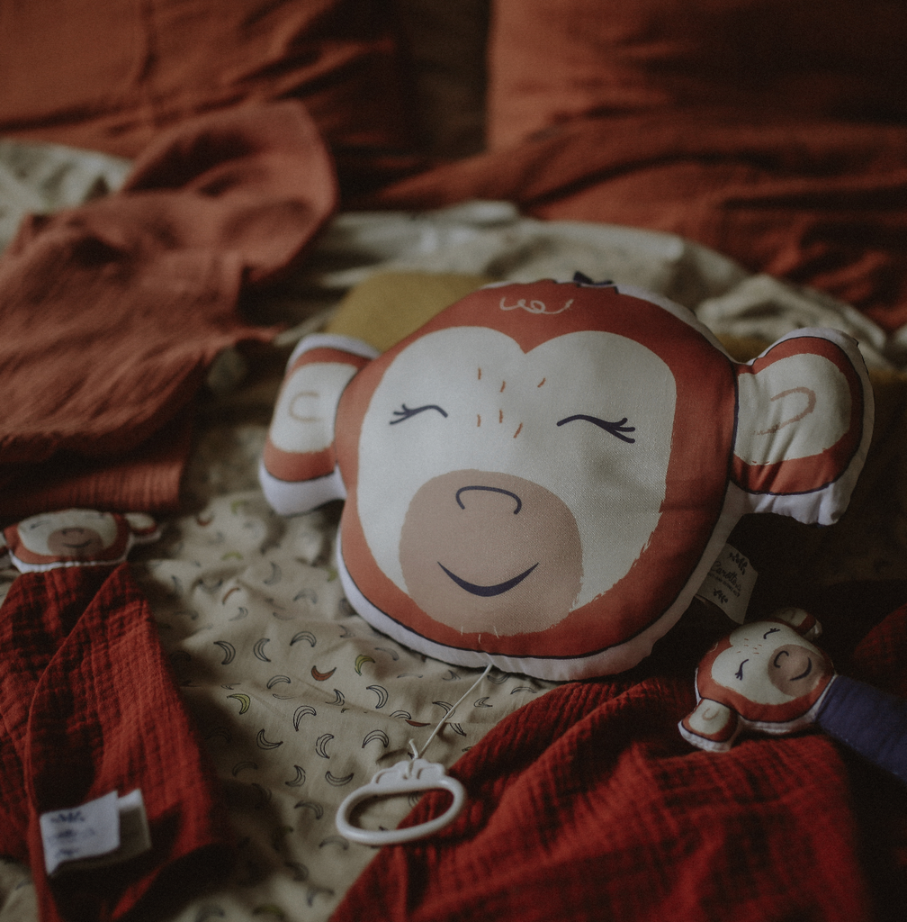 bébé jouant avec son coussin musical illustré motif exclusif tête de singe rouge terracotta Carotte & Cie