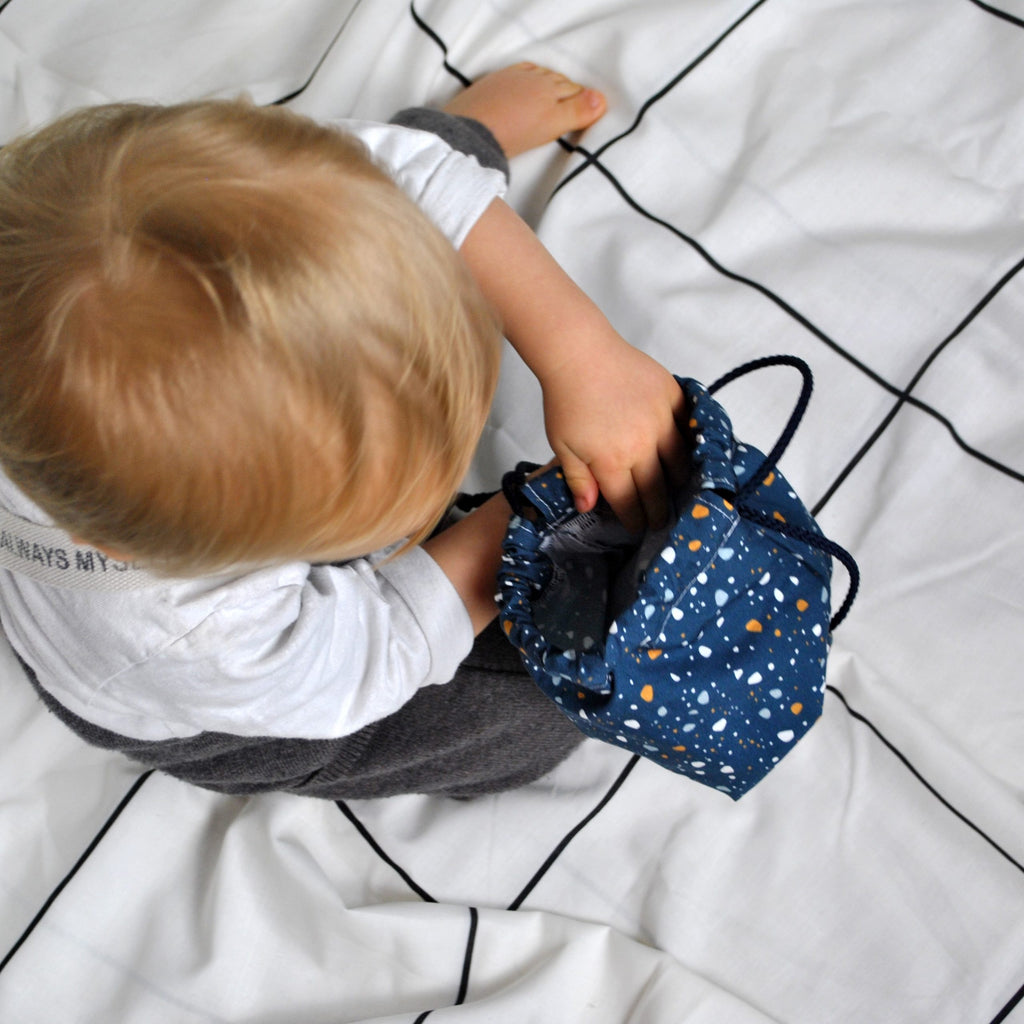 bébé range ses petites affaires dans son pochon en coton avec liens pour le goûter, le pyjama ou les jouets motif granite Terrazzo fond bleu marine Carotte & Cie